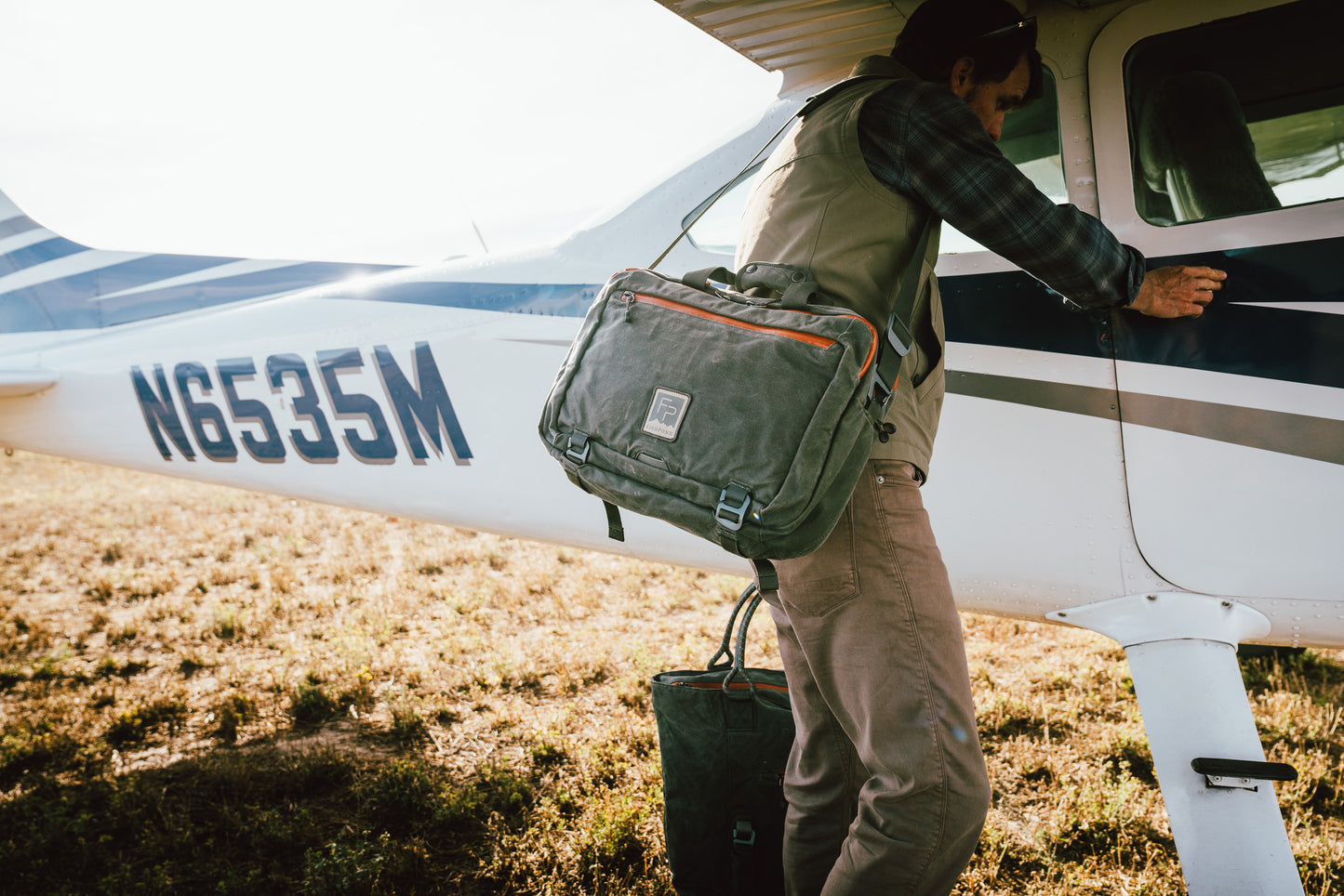 boulder briefcase boarding a small airplane on a grassy field
