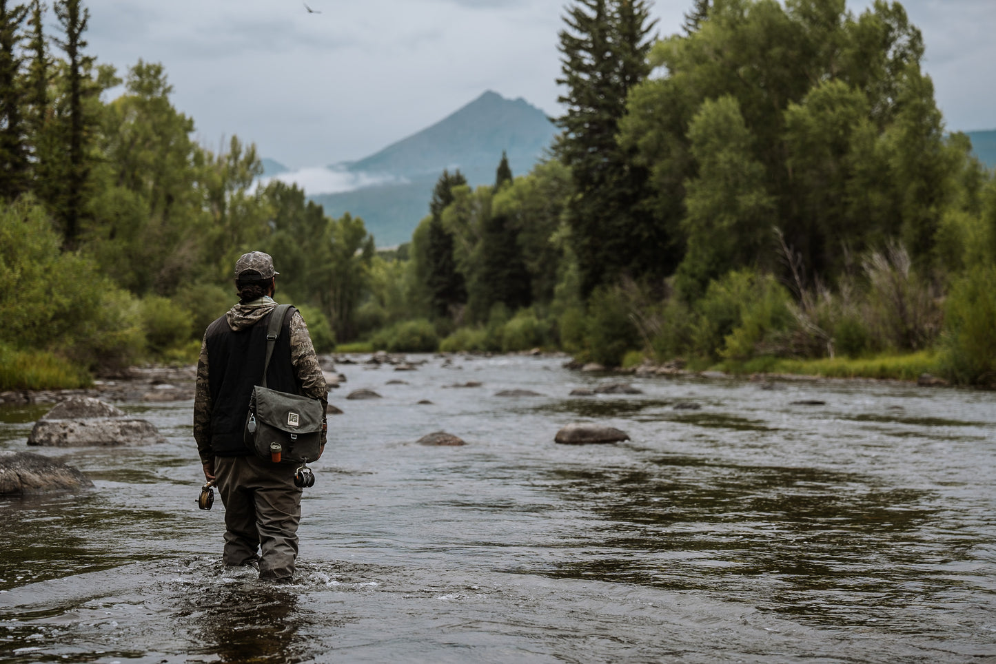 Person walking through a river with mountains and trees in the background